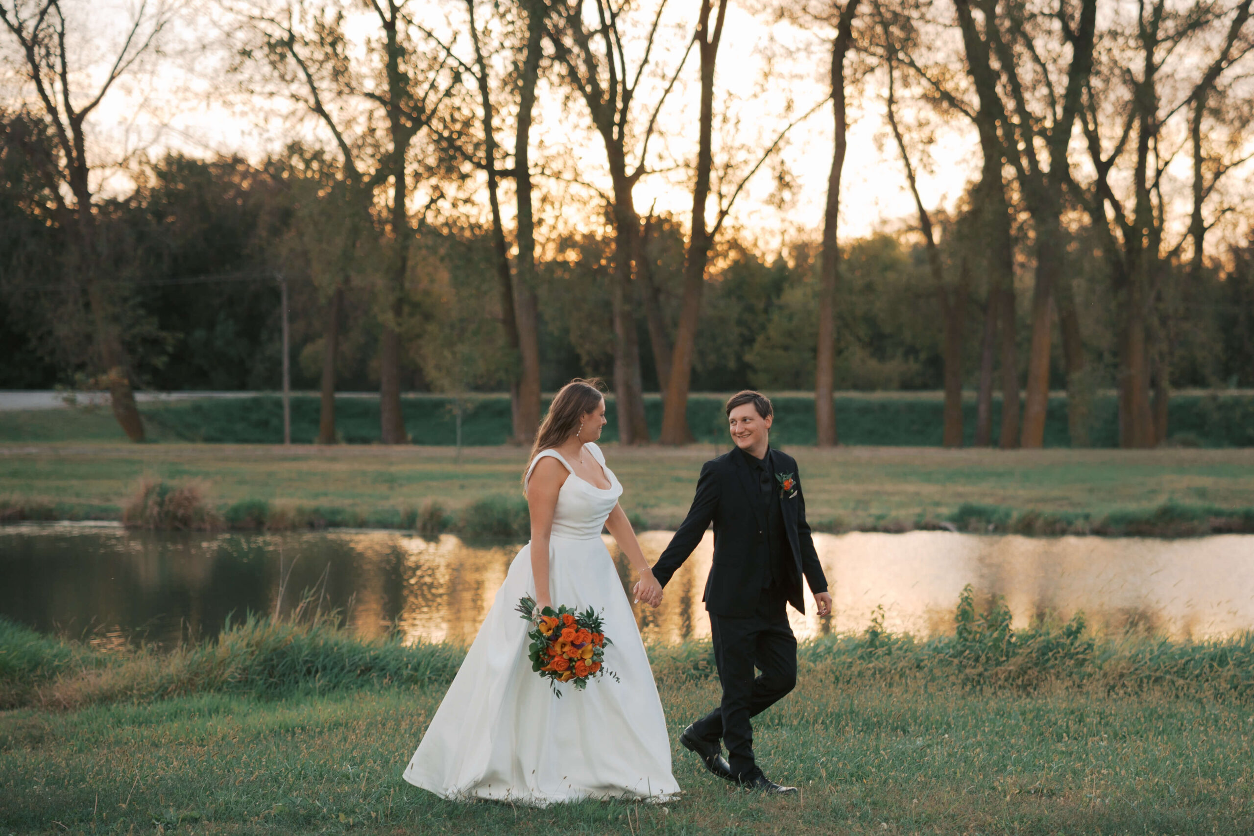 Newlyweds explore one of the lincoln wedding venues ponds at sunset while holding hands