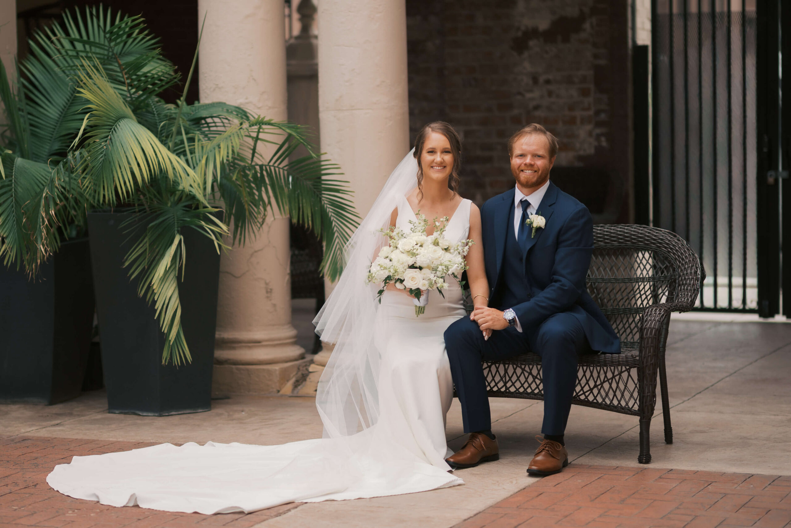 A bride and sits on a wicker bench with her groom in a blue suit with big smiles at one of the lincoln wedding venues