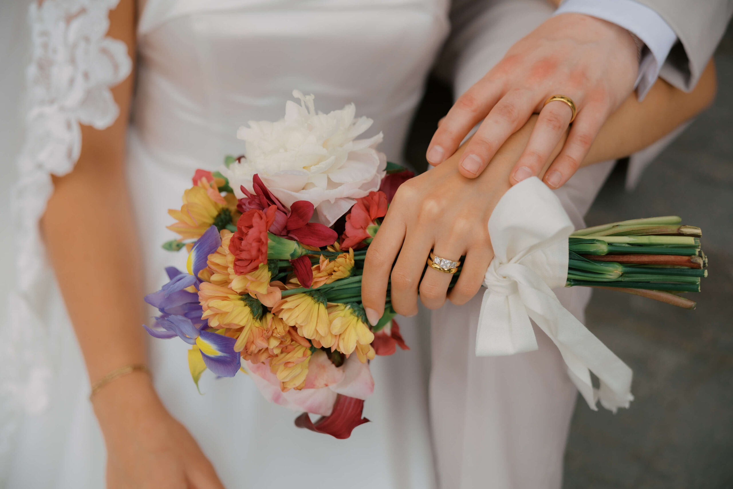 Details of the bride and groom's rings while holding a colorful bouquet