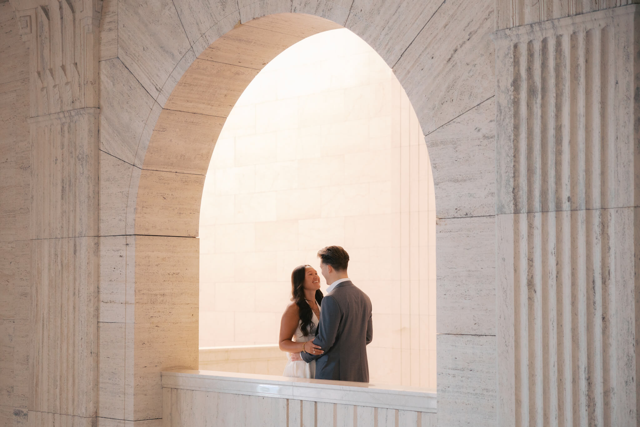 A happy couple smile at each other while snuggling in an archway on a balcony at the joslyn art museum wedding venue