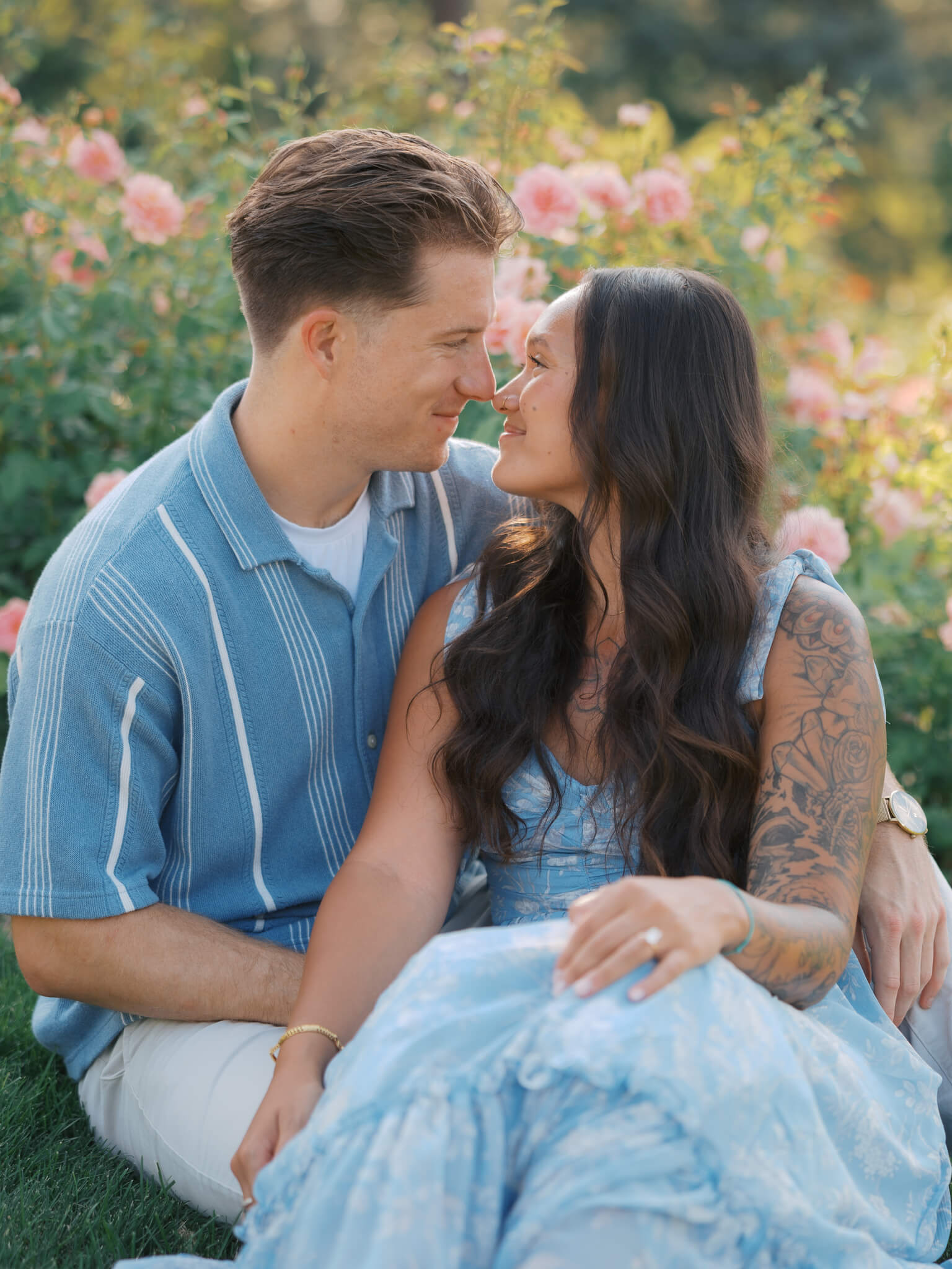 A couple boop noses while snuggling in a garden with pink flowers in blue outfits at the joslyn art museum wedding venue