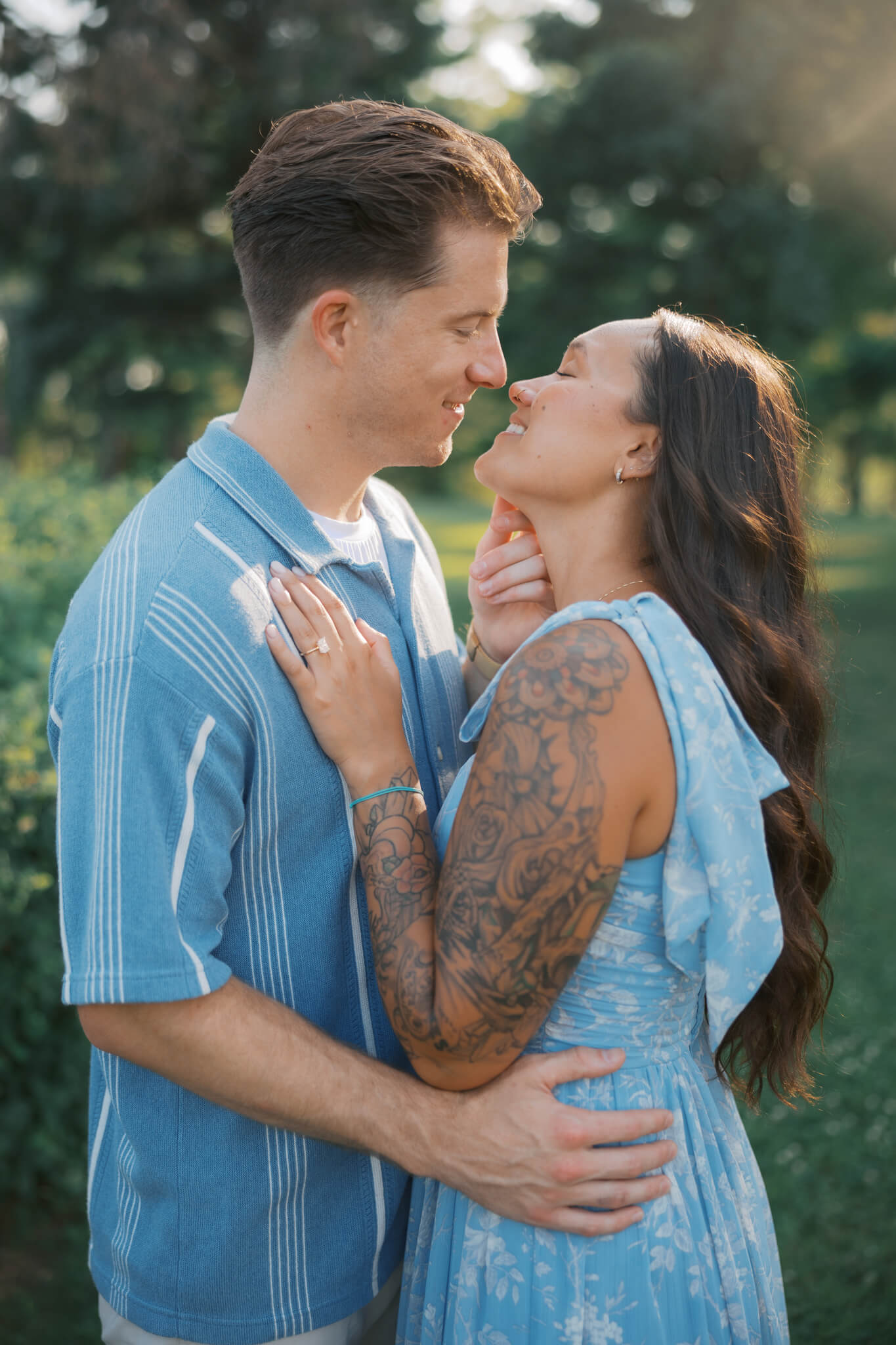 A happy couple in baby blue lean in for a kiss in a garden lawn